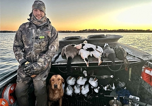  Man standing on boat with dog shows ducks hunted on Gray Goose trip