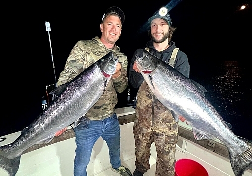 two men pose with large fish at night